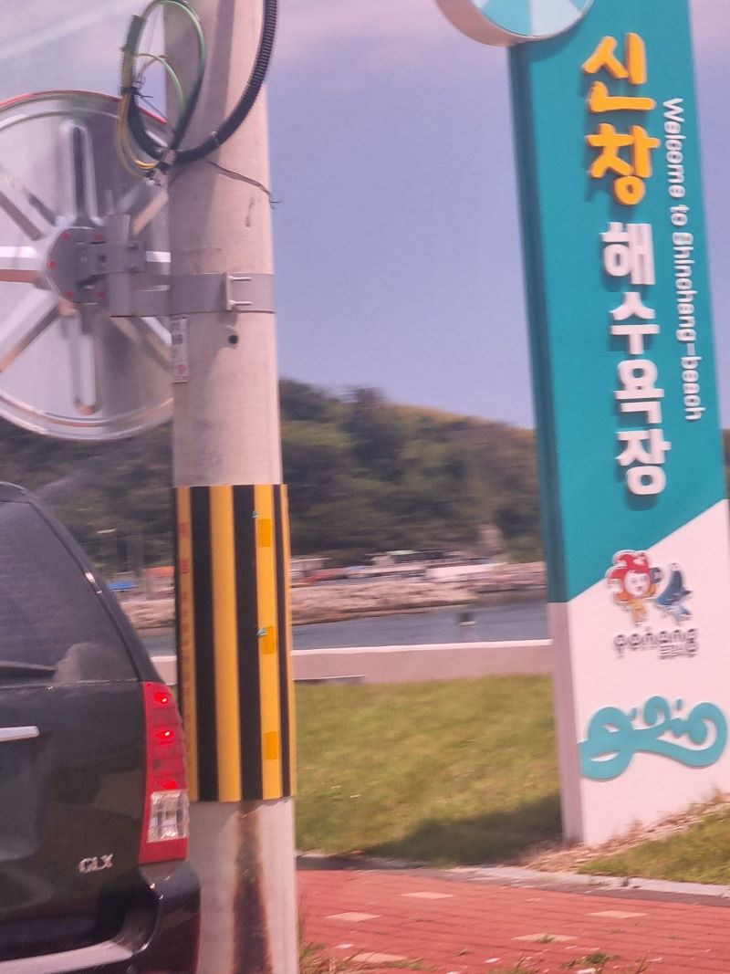 신창 해수욕장 이라 적힌 민트색 입구 표지판과 한적한 어촌 마을 풍경