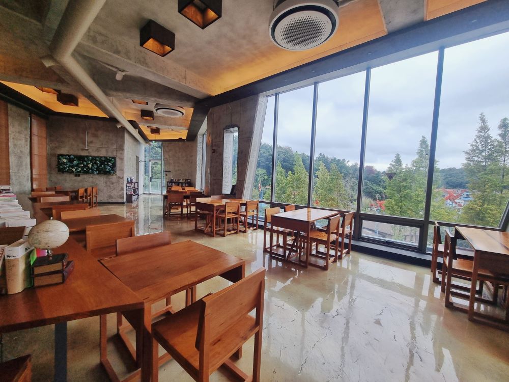 경주 어반산책 카페 2층 통창 너머로 초록빛 숲 뷰와 원목 테이블이 보이는 아늑한 내부 전경