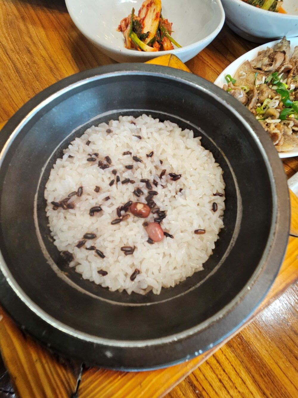 검은색 솥에 흑미와 콩이 얹어진 고소하고 윤기 흐르는 갓 지은 돌솥밥
