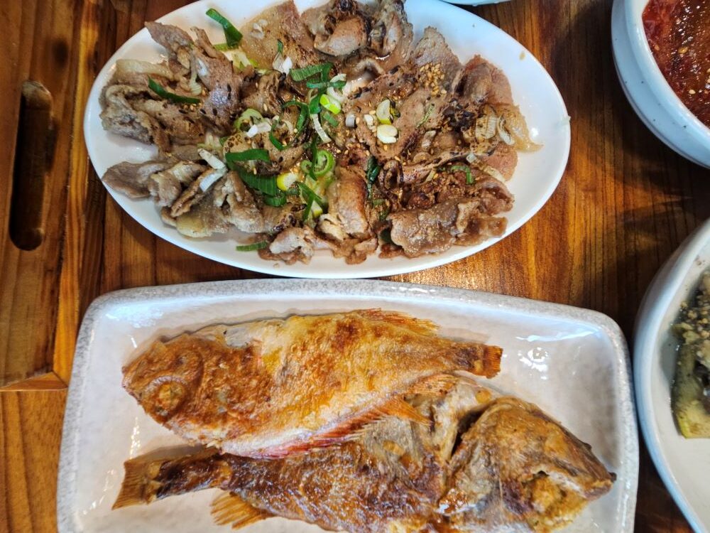 노릇하게 튀기듯 구워낸 생선구이 두 마리와 파와 볶은 돼지 숯불불고기